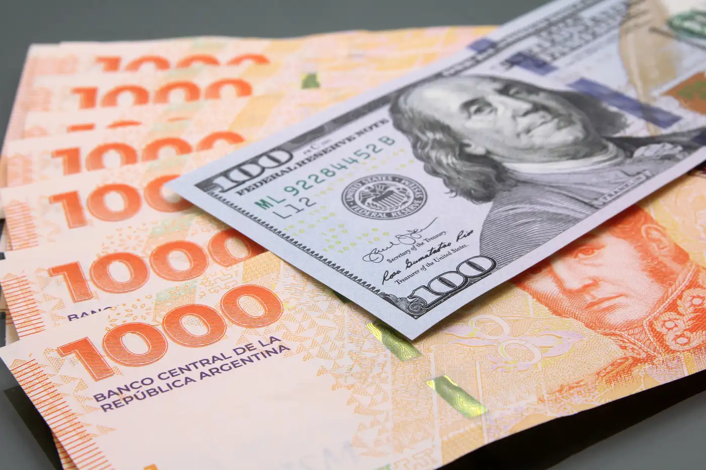 billete dólar sobre billetes de pesos argentinos representando la paridad cambiaria